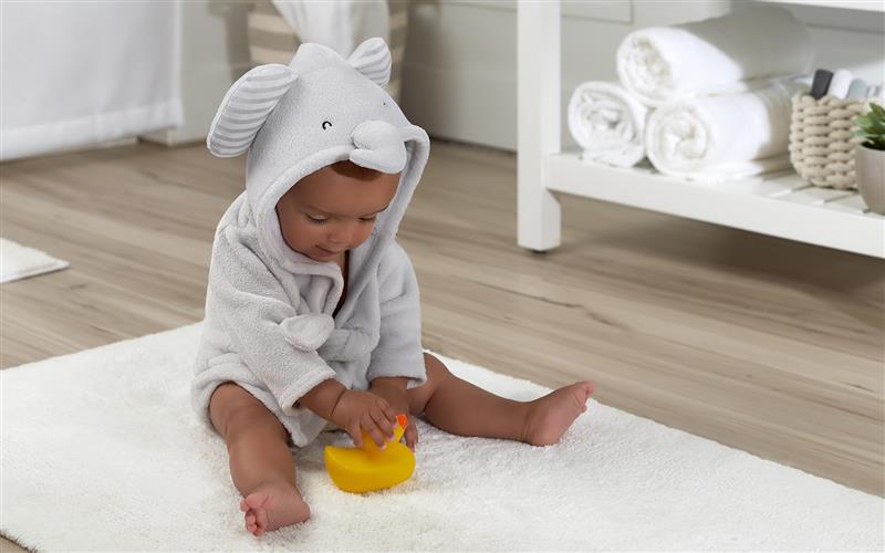 baby sitting in hooded elephant towel on bathroom rug playing with rubber duck