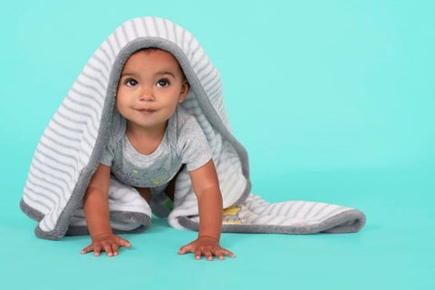 Brown skinned baby with dark eyes crawling on aqua blue floor and wearing a blanket on their head