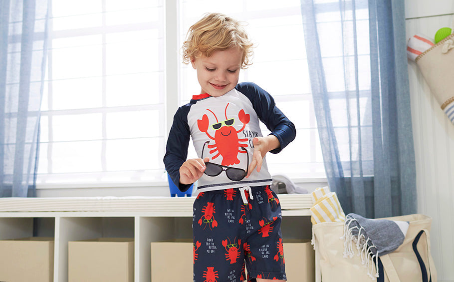 boy holding sunglasses wearing swim trunks