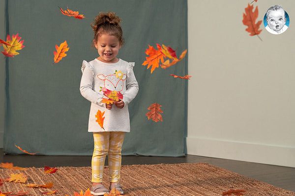 Little girl with yellow leggings playing with autumn leaves.