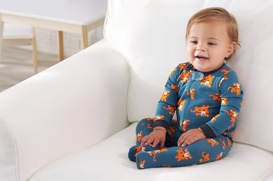 Small child wearing fall pajamas sitting on a white couch.