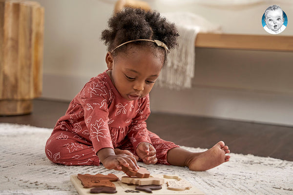 The picture shows a child playing with wooden blocks on a cozy rug, developing her problem-solving abilities and spatial awareness.