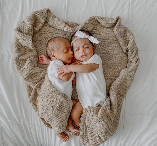 Twin newborn babies hug each other lying down on heart-shaped blanket