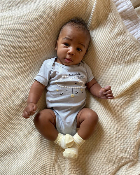 Baby boy wearing gray Onesies bodysuit with yellow socks lying down on bed