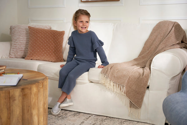 With a smile on her face, a little girl enjoys a comfy moment on the couch with her trusty blanket.