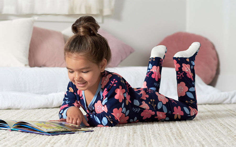 Discover the joy of reading with this little girl in pajamas, lost in the enchanting world of her book.