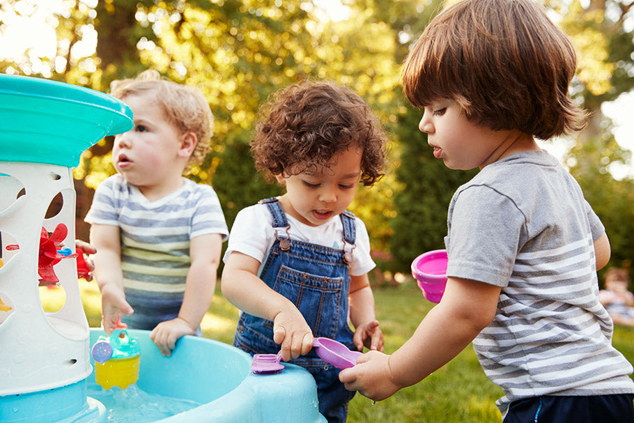 Group Of Young Children Playing With Water Table In Garden