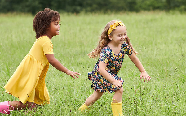 Two girls wearing dresses running in a green field.