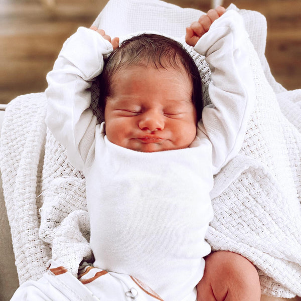 baby sleeping in white shirt with arms raised above head