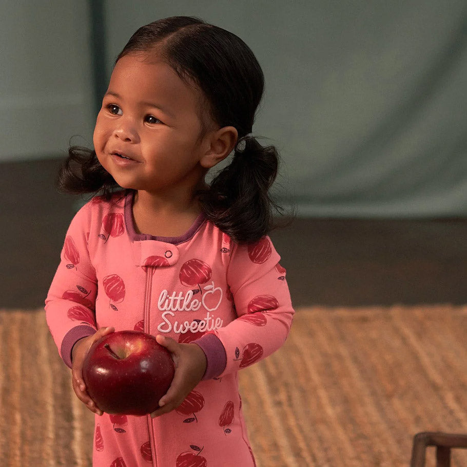 A cute little girl in pink pajamas holds a shiny red apple, ready to take a delicious bite!