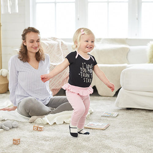 Smiling mom watching her toddler playing in living room