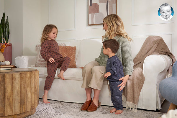 Young blonde mom and her two children sitting on a cream colored couch.