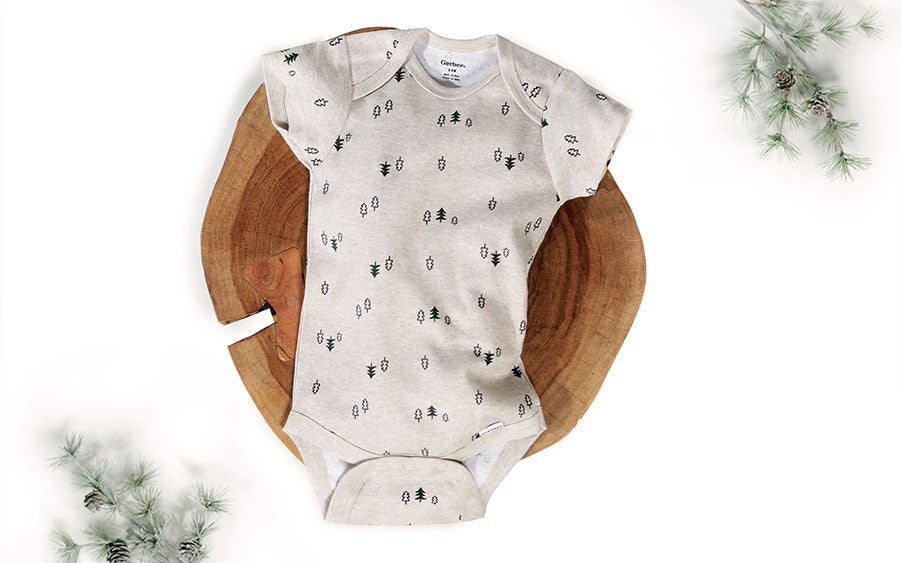 Baby clothing sitting in a natural wooden bowl with holiday spruce twigs.