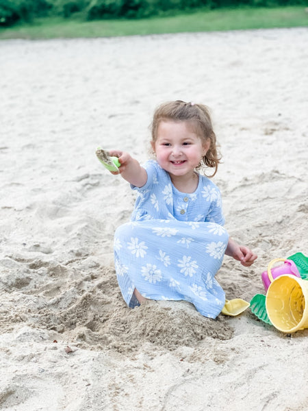 An adorable girl, dressed in beach attire, happily digging and building sandcastles with her trusty shovel and bucket, embracing the joy of childhood playtime.