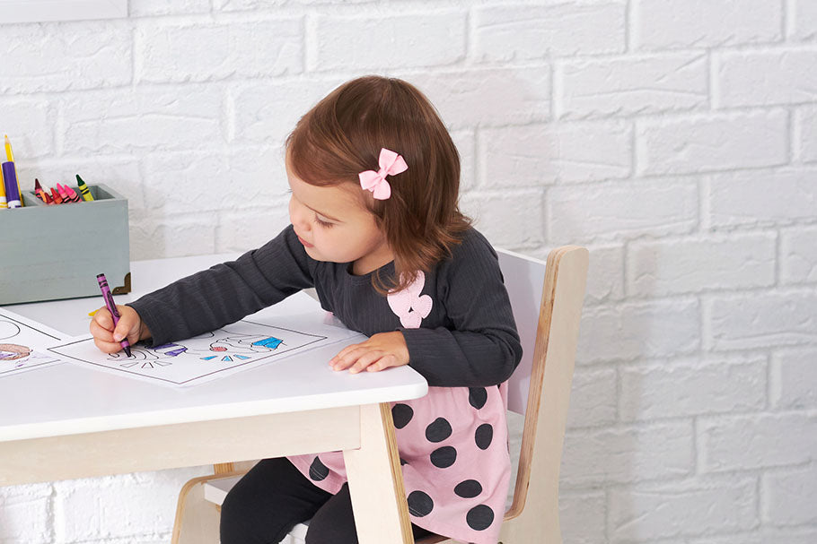 Seated at a table, a young girl is equipped with a pencil and a marker, poised for artistic endeavors.