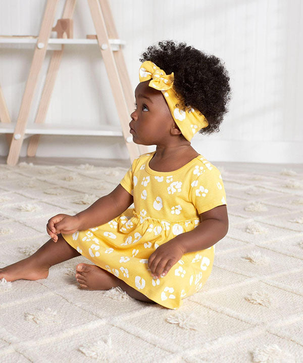 toddler in floral sundress wearing headband sitting on white rug