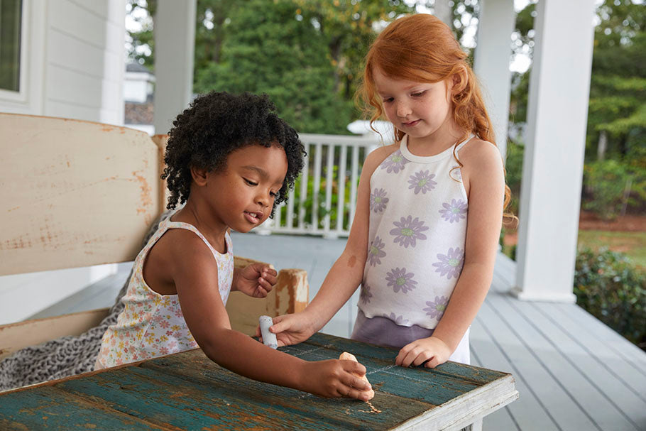A porch serves as the backdrop for two young girls engrossed in playful activities, their innocence shining through.