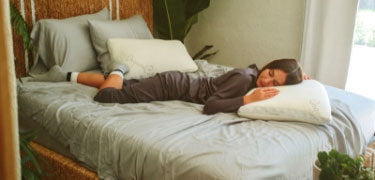 Woman laying on light gray bedding and resting her head on an easy breather natural latex pillow