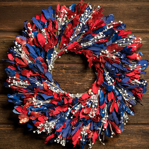 22" botanical wreath is handmade with red and blue integrifolia leaves and white flax on a dark wood background.