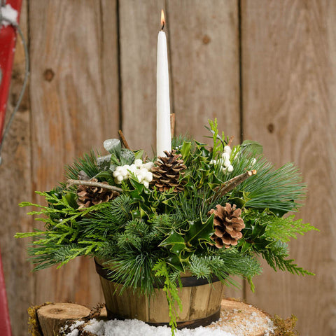 Charming centerpiece in a wooden barrel with holly, pine cones, white berries and a white taper candle close up