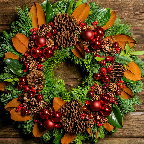 Holiday wreath made of noble fir, cedar, and pine with bay and magnolia leaves, mini pine cones, faux apples and red berries, 5 ponderosa pine cones, 3 large red ball clusters, and 3 small red ball clusters