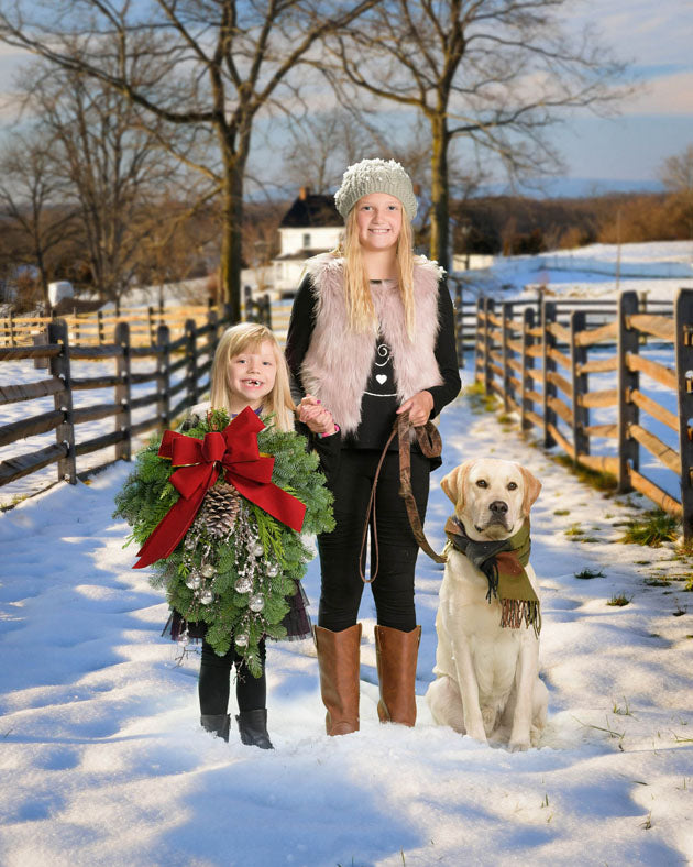 Two young girls, one carrying a wreath, with a yellow labrador retriever