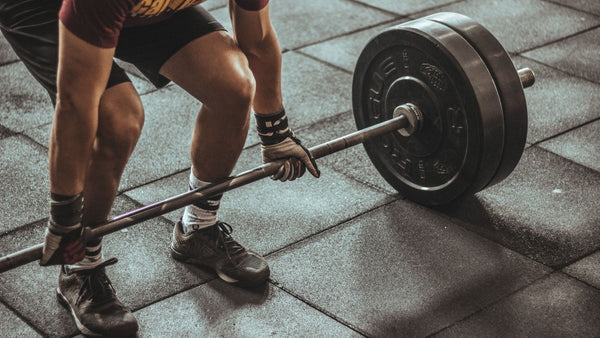 Close up of a man in the gym dead lifting a bar bell with weights on each side wearing grip gloves