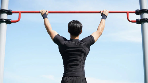 A man hanging from a pull up bar wearing a form fitted athletic black shirt