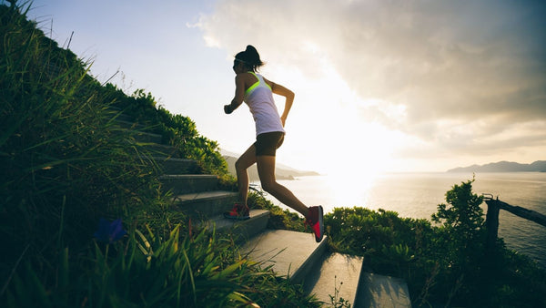 Woman jogging up stone staircase outside, up the side of a mountain