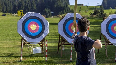 A kid at an archery range releasing an arrow at a target in a field