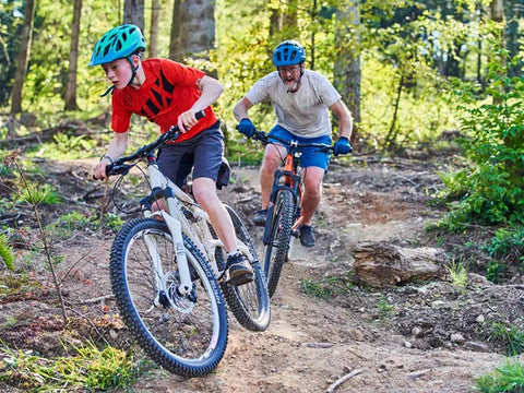 father and son riding on bikes through a forest dirt path