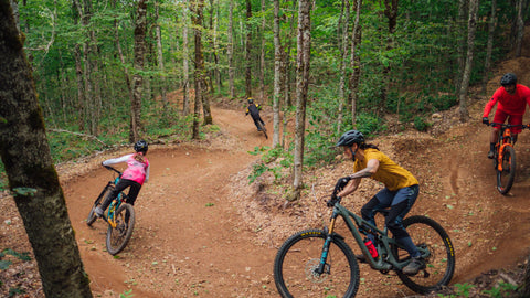 four kids following each other down a forest hill path on bikes