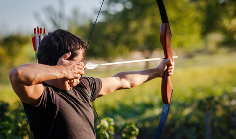 Man with his bow and arrow ready aimed at a target off in the distance