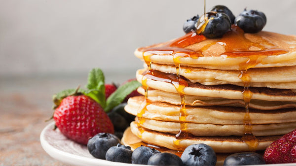 A close up on a stack of pancakes with blueberries and strawberries lining the plate they're on