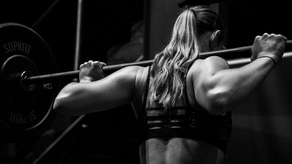 A close up of a woman's back as she squats with the bar bell on her shoulders