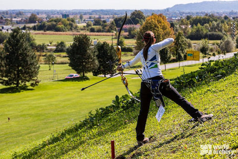 Girl aiming her arrow down hill at an archery range in a field