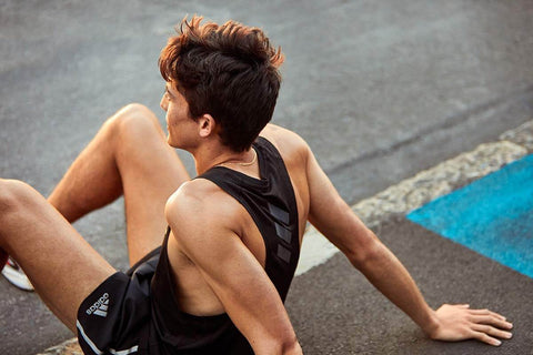 man sitting on pavement in athletic wear staring off at the sun set