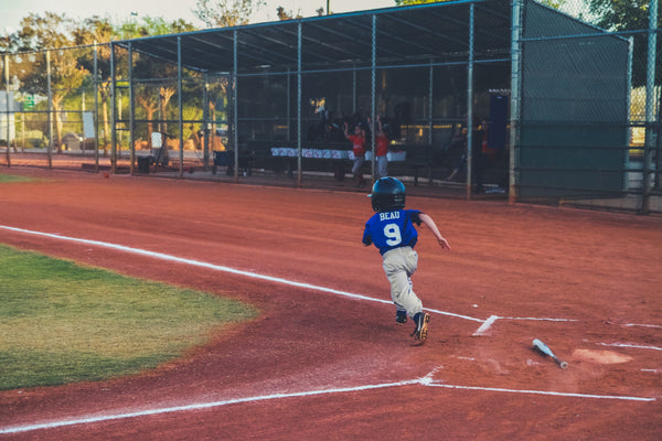 little kid running past home plate after hitting the baseball ball