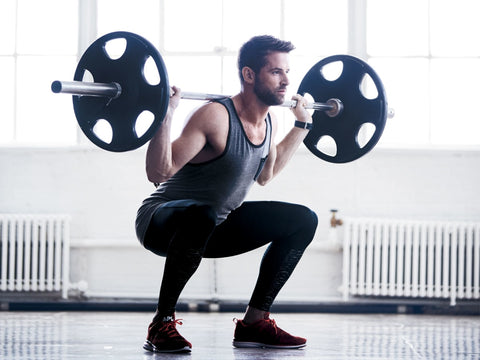 Man in a gym deep squatting a bar bell with weights on it