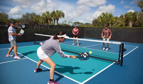 A group of 4 adults playing pickle ball on a court, mid action