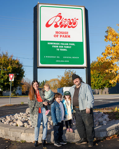 Matty Matheson and family standing in front of tall restaurant sign reading Rizzo's House of Parm