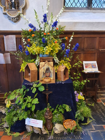 Display of flowers, sponsored by the Friends of Julian, including wooden sculptures of the saint at the foot of an array of summer flowers.
