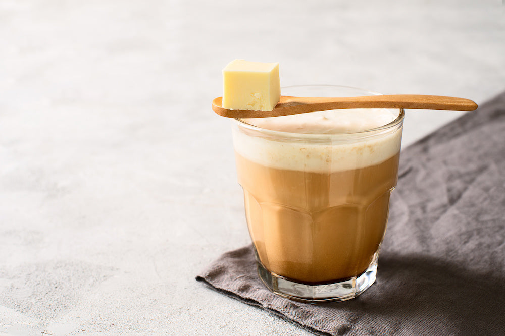 A glass of coffee with a wooden spoon on top containing a cube of butter