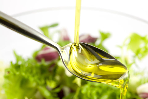 Oil being poured on a spoon with salad in the background