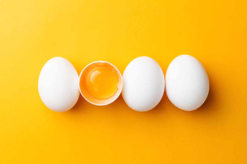 Egg yolk inside a cracked egg shell and three white eggs against a yellow orange background