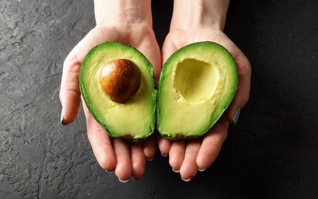 avocado oil: Woman's hands holding two halves of an avocado