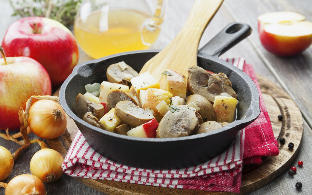 Kidney stew with apples on a cast iron pan surrounded by ingredients