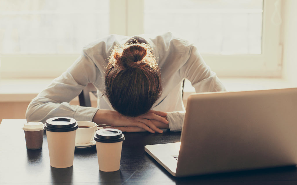 Ketosis symptoms: Stressed woman slumping on the table with cups of coffee and laptop
