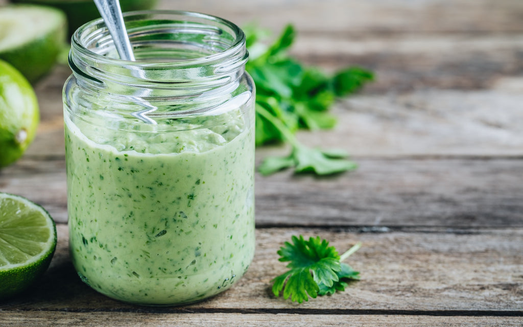 Salad dressing in a glass jar with lime, avocado and cilantro on a wooden surface