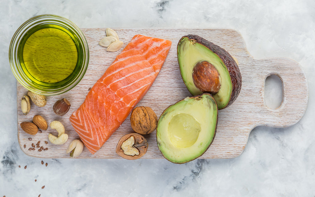 Cutting diet: Raw salmon, avocado, jar of oil, and nuts on a cutting board